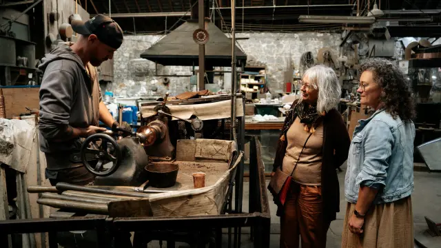 Deux femmes observent une démonstration de repoussage à l'Atelier du Cuivre