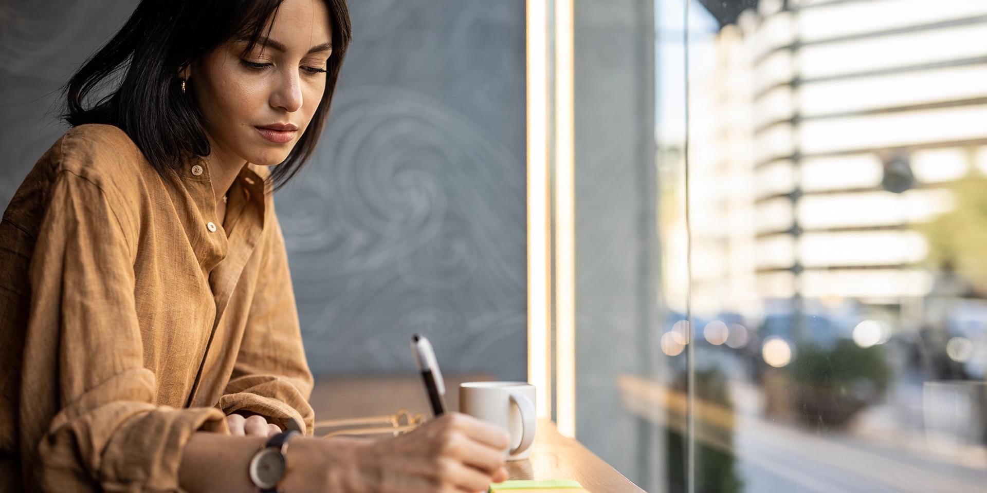 A business woman sits in a cafe by the window and works, writes a reminder in her notebook