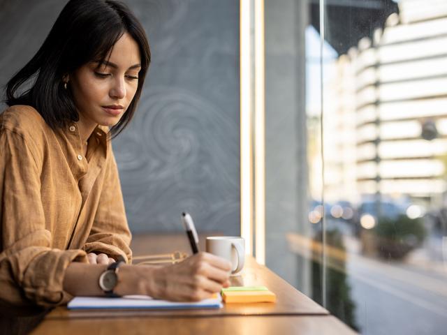 A business woman sits in a cafe by the window and works, writes a reminder in her notebook