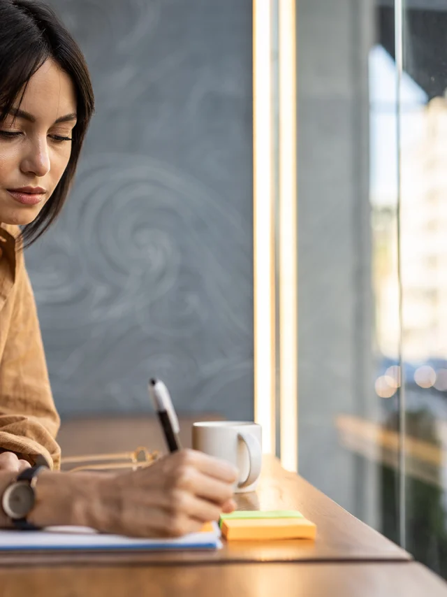 A business woman sits in a cafe by the window and works, writes a reminder in her notebook